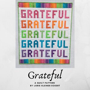 May include: A quilt pattern called "Grateful" by Lorie Kleiner Eckert. The pattern features the word "Grateful" repeated five times in different colors, including pink, orange, green, blue, and purple. The background is white with a small, white, patterned design.