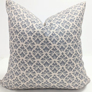 May include: A square throw cushion featuring a repeating pattern of slate blue stylised floral motifs set against a cream-coloured background. The fabric has a visible woven texture, and the cushion is plumped to create a structured, upright shape.