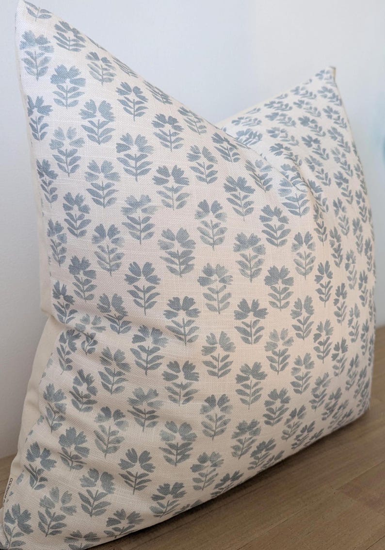 May include: A white cushion with a blue floral pattern. The cushion is made of a soft, textured fabric.