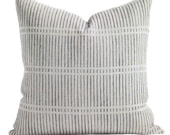 May include: A square throw cushion featuring a textured off-white fabric base with a repeating pattern of vertical dark grey stripes. The design includes horizontal bands that intersect the vertical lines, creating a structured grid-like appearance.