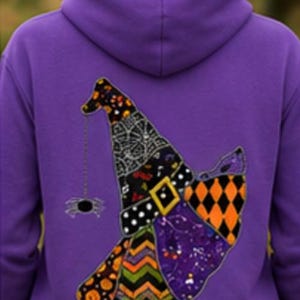 May include: A purple hooded sweatshirt featuring a large graphic on the back of a witch hat. The hat is composed of various patterned patches including orange and black diamonds, green and orange chevrons, and a spider hanging from the tip.