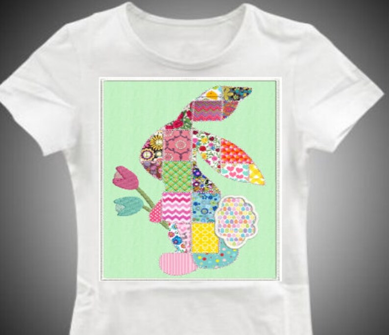 Puede incluir: Una camiseta blanca con un dise&ntilde;o de conejo de patchwork colorido en la parte delantera. El conejo est&aacute; hecho de cuadrados de tela de diferentes colores y tiene una flor rosa detr&aacute;s.