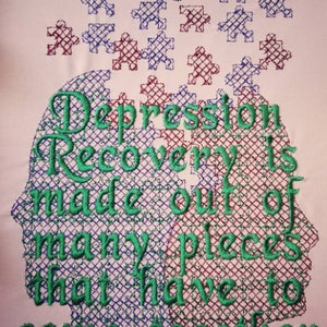 May include: Green embroidered text on a white background reads "Depression Recovery is made out of many pieces that have to come together". The text is inside a silhouette of a human head made of puzzle pieces.
