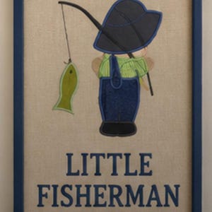 May include: A framed wall art piece featuring an embroidered applique of a figure wearing a dark blue hat and overalls, holding a fishing rod with a green fish attached. The text "LITTLE FISHERMAN" is embroidered in dark blue below the figure.