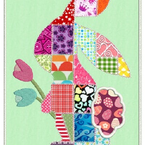 Puede incluir: Un conejito de patchwork con una flor en la boca. El conejito est&aacute; hecho de diferentes telas de colores con varios patrones, incluyendo lunares, rayas y corazones. El fondo es de color verde claro.
