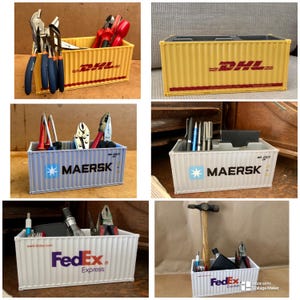 May include: Four miniature shipping containers, each with a different company logo, are used as desk organisers. The containers are filled with various office supplies, such as pens, pencils, and tools. The containers are yellow, grey, blue, and white.