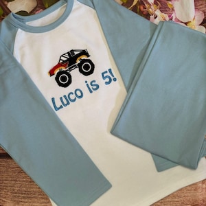 May include: A white and light blue long-sleeved shirt with a monster truck graphic and the text "Luco is 5!" embroidered on the front.