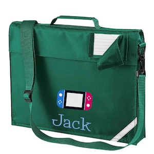 Könnte beinhalten: Eine grüne Schultasche mit einem Schultergurt und einer Tasche auf der Vorderseite. Die Tasche hat ein weißes Namensschild mit dem Namen "Jack" und eine bunte Grafik eines Videospiel-Controllers.