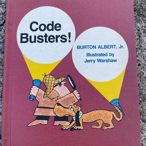 以下が含まれることがあります： 白い文字で「Code Busters!」というタイトルが書かれた赤い本の表紙。本は、懐中電灯を持った漫画の探偵と犬が描かれています。