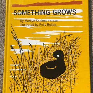 Puede incluir: Una cubierta de libro amarilla con el título "SOMETHING GROWS" en texto negro. El libro es de Marilyn Schima, R.N., Ed.D. e ilustrado por Polly Bolian. La cubierta presenta una silueta negra de un patito en un campo de hierba alta.
