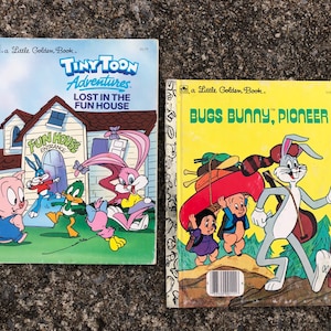 May include: Two vintage Little Golden Books. The first book is titled "Tiny Toon Adventures Lost in the Fun House" and features a cartoon house with a pink rabbit, a blue rabbit, a pig, and a duck. The second book is titled "Bugs Bunny, Pioneer" and features Bugs Bunny carrying a canoe and a raccoon on his back.