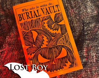 May include: An orange rectangular book cover featuring black ink illustrations of three jack-o'-lanterns with jagged, triangular eyes and mouths. The text reads "What tales lie within the... BURIAL VAULT" and "LOST BOY" on a white bat shape.