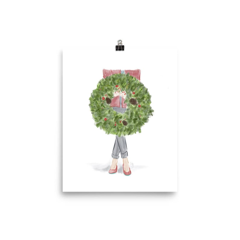 May include: A woman in a red sweater and blue jeans holds a green Christmas wreath in front of her.