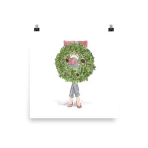 May include: A watercolor illustration of a person wearing a red sweater and jeans standing behind a green Christmas wreath.