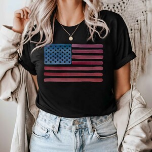May include: A black t-shirt with a watercolor-style American flag design. The flag is in shades of red, white, and blue.