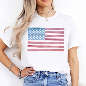 May include: White t-shirt with a watercolor American flag design. The flag is in shades of blue and red.
