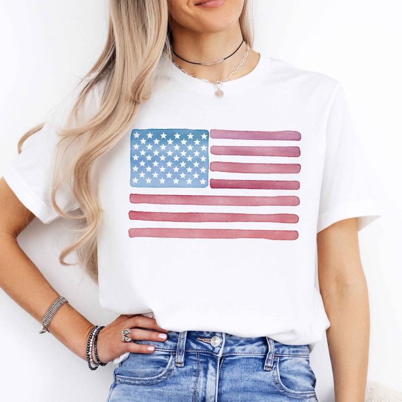 May include: White t-shirt with a watercolor American flag design. The flag is in shades of blue and red.