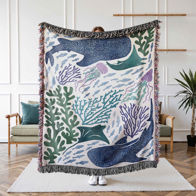 K&ouml;nnte beinhalten: Eine gewebte Tapisserie-Decke mit einer farbenfrohen Unterwasser-Szene mit einem Walhai, Rochen, Korallen, Quallen und Fischen. Die Decke hat einen wei&szlig;en Hintergrund mit blauen, gr&uuml;nen und violetten Akzenten.