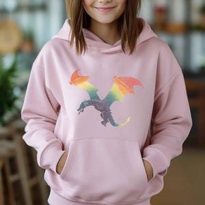 K&ouml;nnte beinhalten: Ein rosa Hoodie mit einem Regenbogen-Drachen-Motiv. Der Drache fliegt mit ausgebreiteten Fl&uuml;geln.