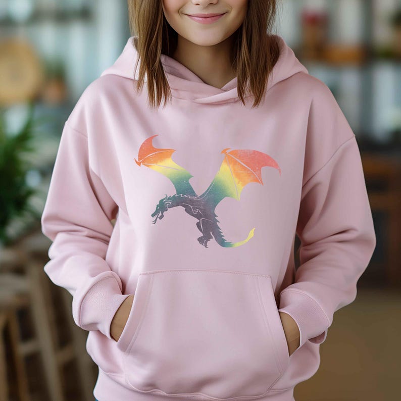 K&ouml;nnte beinhalten: Ein rosa Hoodie mit einem Regenbogen-Drachen-Motiv. Der Drache fliegt mit ausgebreiteten Fl&uuml;geln.