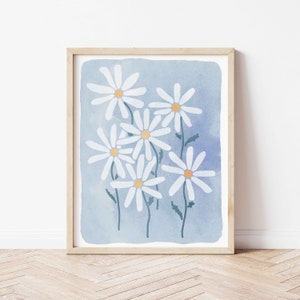 May include: A framed print of a watercolor painting featuring a cluster of white daisies with yellow centers on a light blue background.