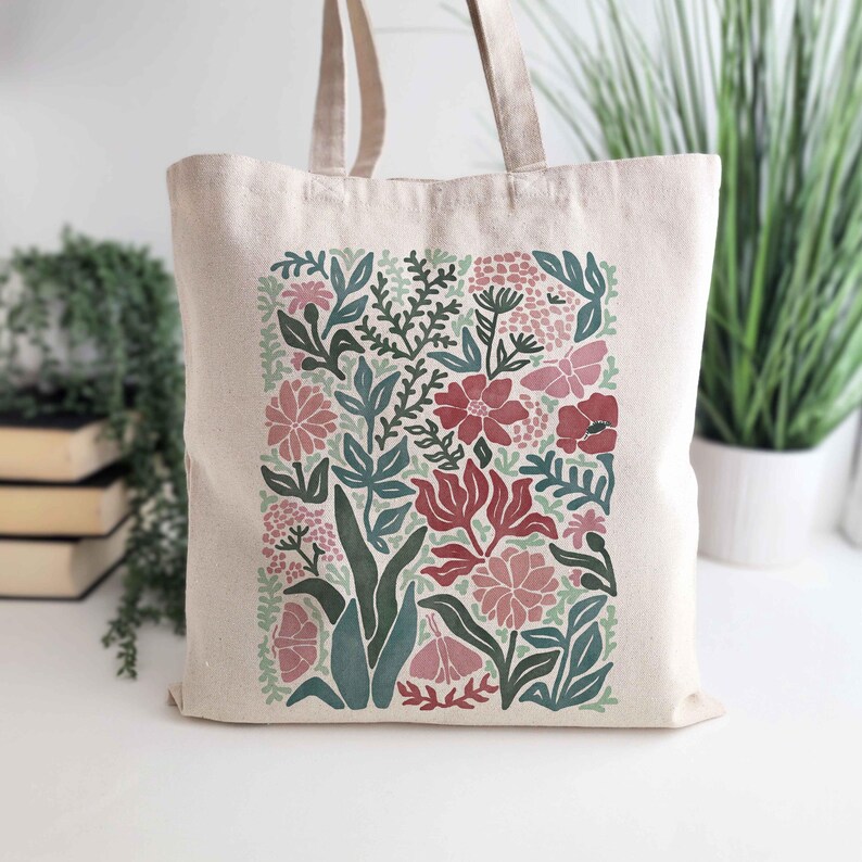 K&ouml;nnte beinhalten: Beige Canvas-Tragetasche mit floralem Design. Das Design umfasst rote, rosa und gr&uuml;ne Blumen und Bl&auml;tter. Die Tragetasche hat zwei beige Griffe und eignet sich zum Tragen von Lebensmitteln oder anderen Gegenst&auml;nden.