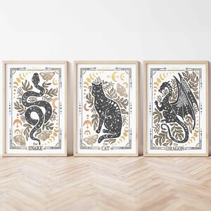 K&ouml;nnte beinhalten: Drei gerahmte Drucke mit einer schwarzen und wei&szlig;en Silhouette einer Schlange, einer Katze und eines Drachen. Jeder Druck hat einen goldenen und braunen Hintergrund mit einem floralen Design und den Text "the snake", "the cat" und "the dragon".