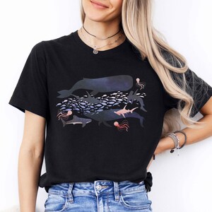K&ouml;nnte beinhalten: Schwarzes T-Shirt mit einem grafischen Druck eines Wals, Hais, Fische und Quallen in Blaut&ouml;nen, Rosa und Lila.