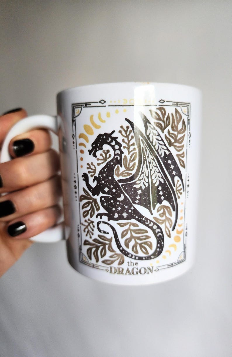 Watercolor celestial dragon mug featuring a mystical dragon surrounded by stars, moons, and botanical elements, framed with an elegant tarot-style border — fantasy-inspired boho coffee cup design.