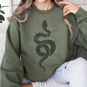 May include: A green sweatshirt with a black snake design. The snake is surrounded by leaves and has a starry pattern.