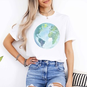 May include: A white t-shirt with a blue and green watercolor globe graphic. The globe is centered on the shirt and has a distressed look.