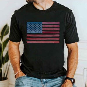 May include: A black t-shirt with a watercolor-style American flag design. The flag is in shades of red, white, and blue.