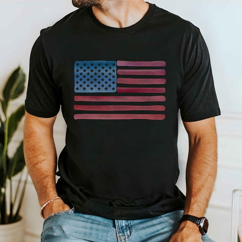 May include: A black t-shirt with a watercolor-style American flag design. The flag is in shades of red, white, and blue.