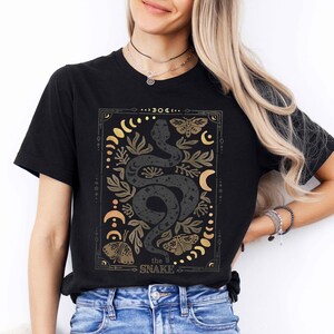 May include: Black t-shirt with a gold and black graphic design of a snake with moons, stars, and butterflies. The text "the SNAKE" is at the bottom of the design.
