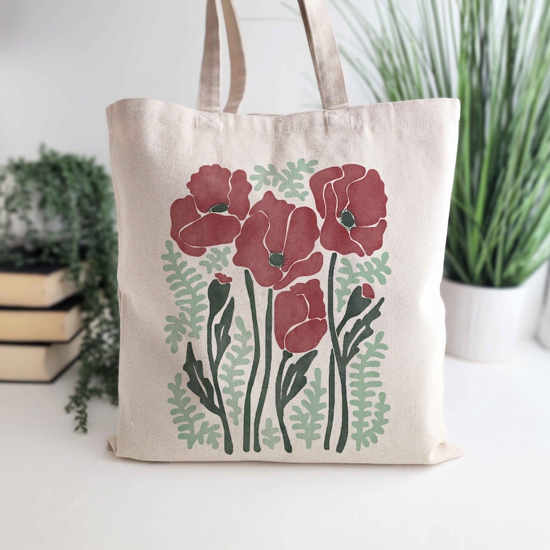 A whimsical canvas tote bag featuring vibrant red poppies and delicate light green botanical elements. This nature-inspired design blends floral elegance with a touch of whimsy, perfect for flower lovers, gardeners, and botanical enthusiasts. Ideal for everyday use, shopping, or as a unique gift