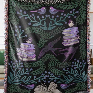 A woven blanket featuring a whimsical dark fantasy design of birds, books, and botanical elements in shades of green, purple, and blue. Available with a white or black background, the intricate illustration resembles a storybook or enchanted library scene, perfect for book lovers. The high-quality woven fabric adds texture and warmth, making it ideal as a cozy throw, reading nook accent, or wall tapestry