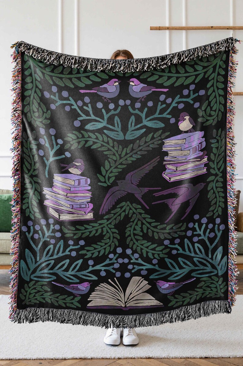 A woven blanket featuring a whimsical dark fantasy design of birds, books, and botanical elements in shades of green, purple, and blue. Available with a white or black background, the intricate illustration resembles a storybook or enchanted library scene, perfect for book lovers. The high-quality woven fabric adds texture and warmth, making it ideal as a cozy throw, reading nook accent, or wall tapestry