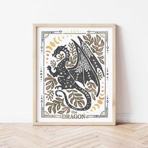 K&ouml;nnte beinhalten: Eine Schwarzwei&szlig;illustration eines Drachen mit goldenen und braunen Akzenten. Der Drache ist von Bl&auml;ttern und Mondsicheln umgeben. Der Text "the DRAGON" befindet sich am unteren Rand des Bildes.
