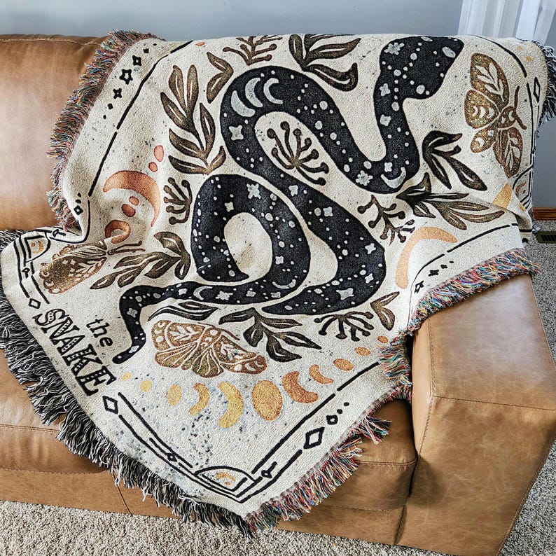 A mystical woven blanket featuring a celestial snake design filled with moons and stars, surrounded by botanical elements, crescent moons, and twinkling stars in an intricate tarot-inspired border. The rich, detailed artwork creates a witchy, astrology-inspired aesthetic, perfect for adding a magical and mystical touch to any space. Ideal as a cozy throw, bedspread, or statement wall tapestry for those who love tarot, celestial themes, and occult decor