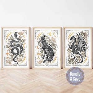 K&ouml;nnte beinhalten: Drei gerahmte Drucke mit einer Schwarzwei&szlig;illustration einer Schlange, einer Katze und eines Drachen. Jeder Druck hat einen goldenen und wei&szlig;en Hintergrund mit den Worten "the snake", "the cat" und "the dragon" unten.