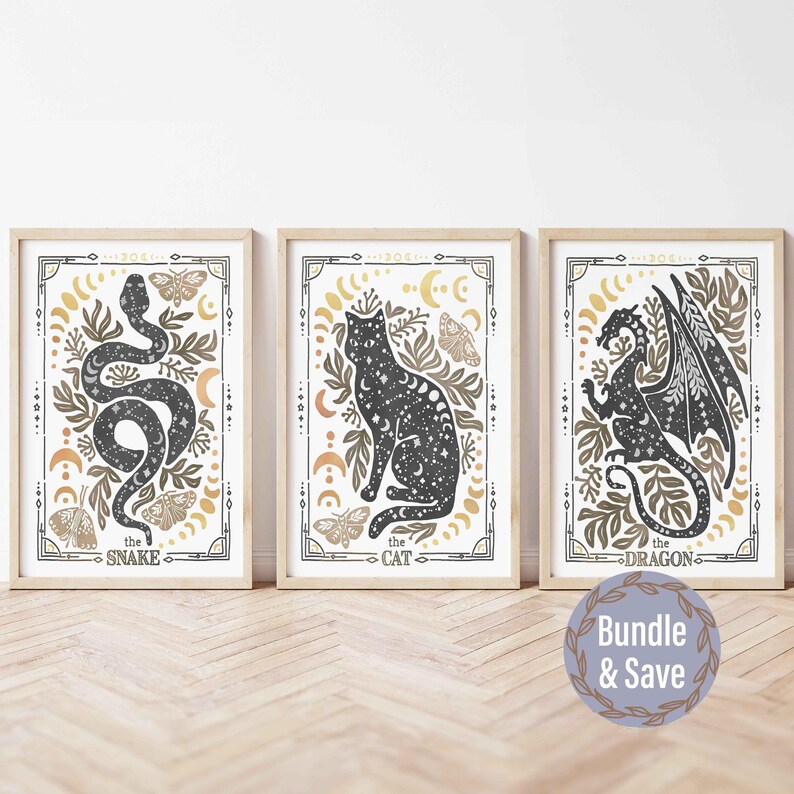 K&ouml;nnte beinhalten: Drei gerahmte Drucke mit einer Schwarzwei&szlig;illustration einer Schlange, einer Katze und eines Drachen. Jeder Druck hat einen goldenen und wei&szlig;en Hintergrund mit den Worten "the snake", "the cat" und "the dragon" unten.