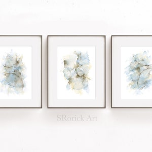 May include: Three framed watercolor paintings with abstract designs in shades of blue and brown. The paintings are displayed on a white wall.