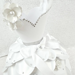 Peut inclure: Bouquet de fleurs en papier blanc avec un ruban de satin blanc et des strass. Le bouquet est en forme de robe et a une jupe à étages.