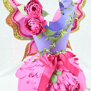 Op de afbeelding: Een roze papieren fee&euml;njurk met een paarse bovenkant, roze bloemen, groene bladeren en een roze satijnen lint. De jurk heeft gouden glittervleugels met roze strass.