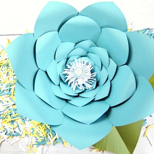 May include: A large, light blue paper flower with a white center. The flower is made of multiple layers of paper and has a green stem.