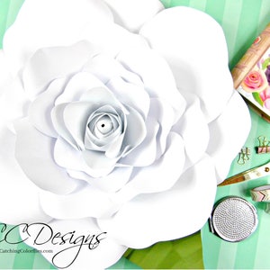 May include: A large white paper flower with a layered center. The flower is on a green and white striped background. The text "CC Designs" and "CatchingColorflies.com" is visible in the bottom left corner of the image.