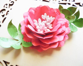 May include: A pink paper flower with white pearl accents and green leaves. The flower is layered and has a delicate, feminine look.
