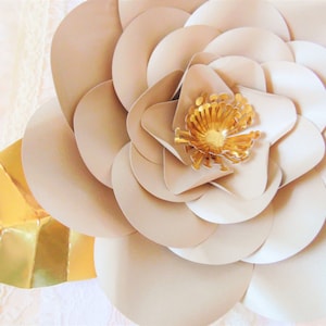 May include: A large, beige paper flower with a gold center. The flower is made of multiple layers of paper, creating a 3D effect.