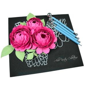 May include: Three pink paper flowers with green leaves on a black surface with white drawn flowers and four blue tools with silver ball tips. The text "Abbi Kirsten Collections" is written in white on the black surface.