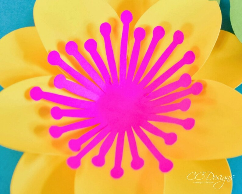 May include: A bright yellow paper flower with a pink center. The center is made of paper and has a starburst design.